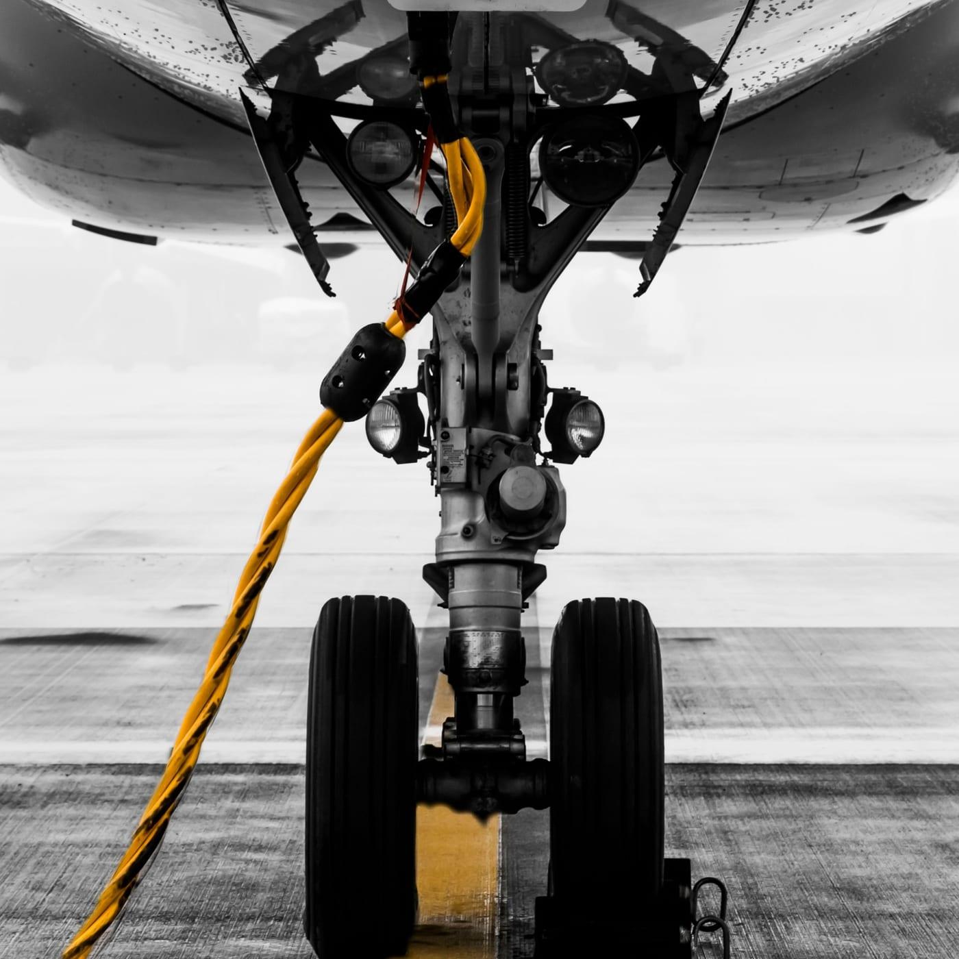 The nose gear of a parked jet head-on, a yellow ground-power cable running in from the left.