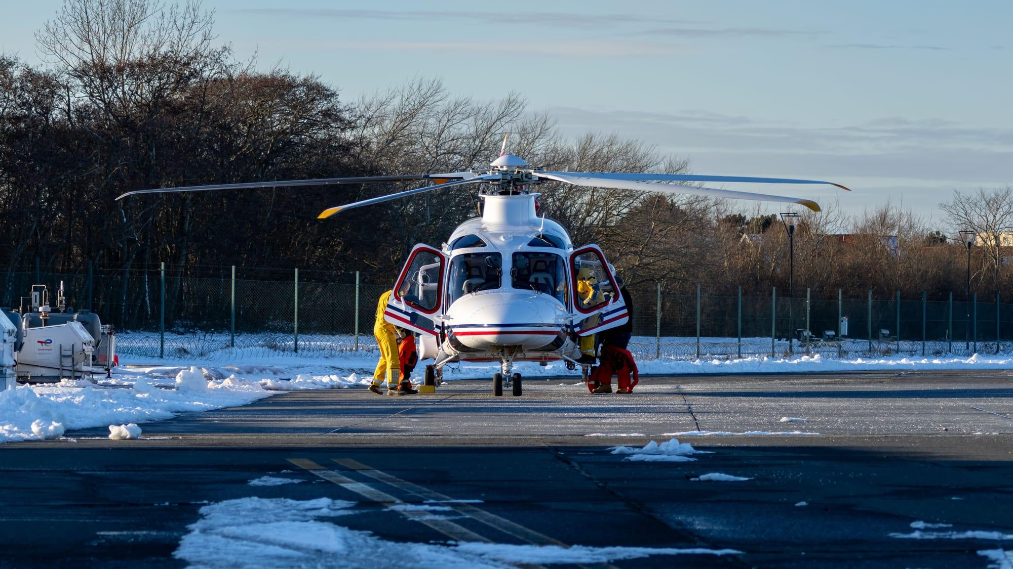 Two crew in hi-vis working at the open doors of a helicopter on a snow-edged ramp.