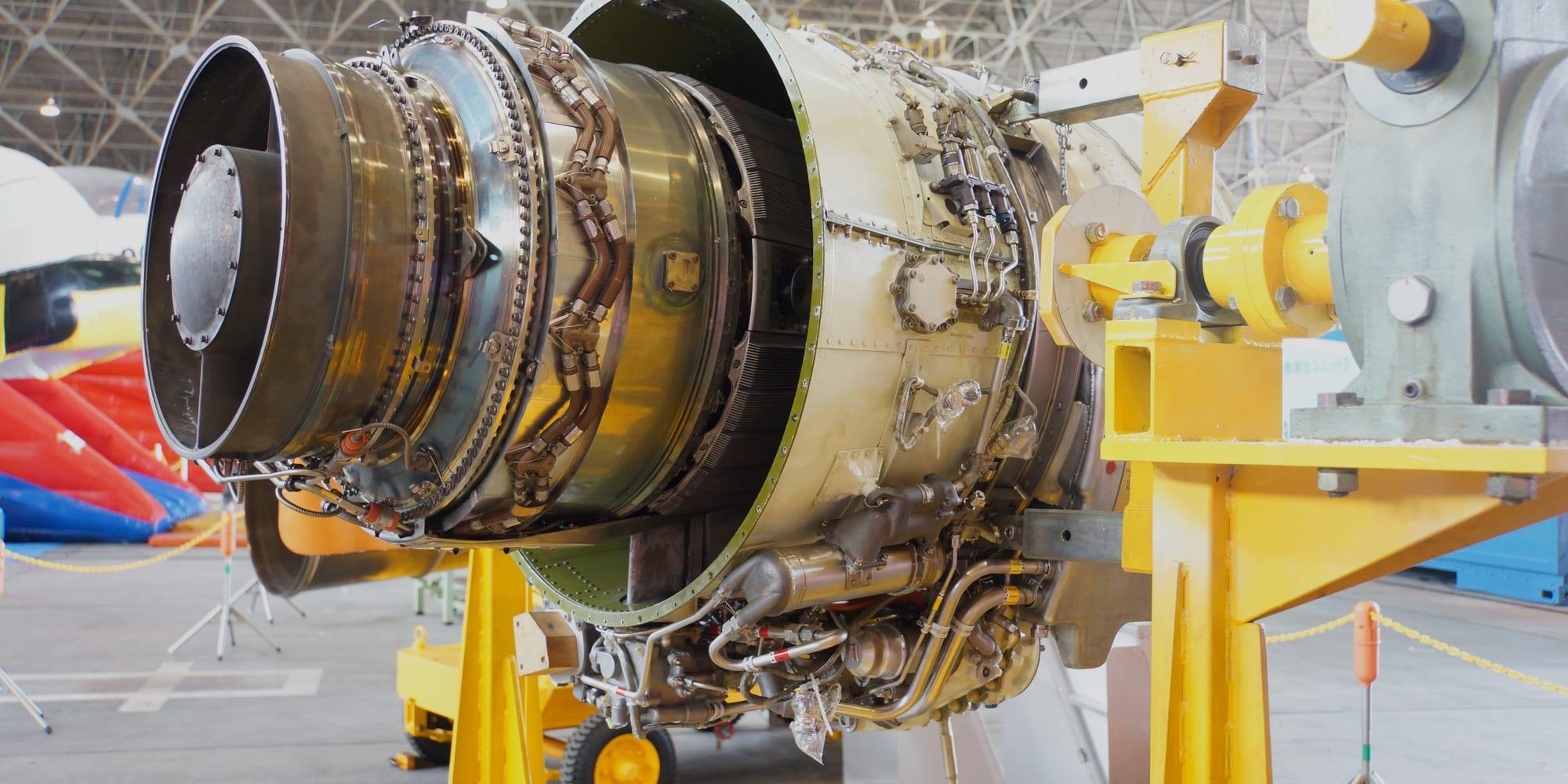 A small turbofan engine bolted to a yellow maintenance stand in a hangar, cowlings off and the fan, fuel manifold and accessory plumbing exposed.