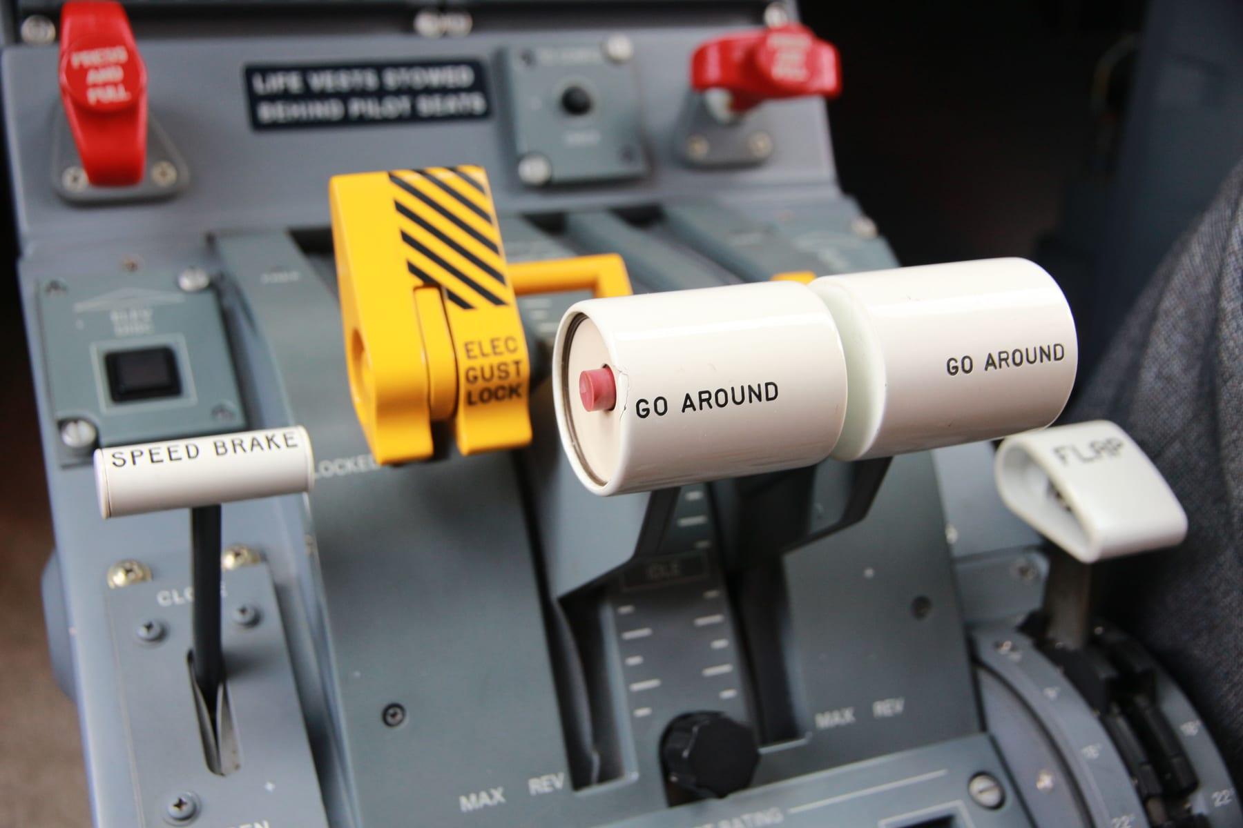 The centre pedestal of an Embraer 145 flight deck: speed brake handle, yellow electric gust lock, and the two power levers with GO AROUND buttons on their tops.
